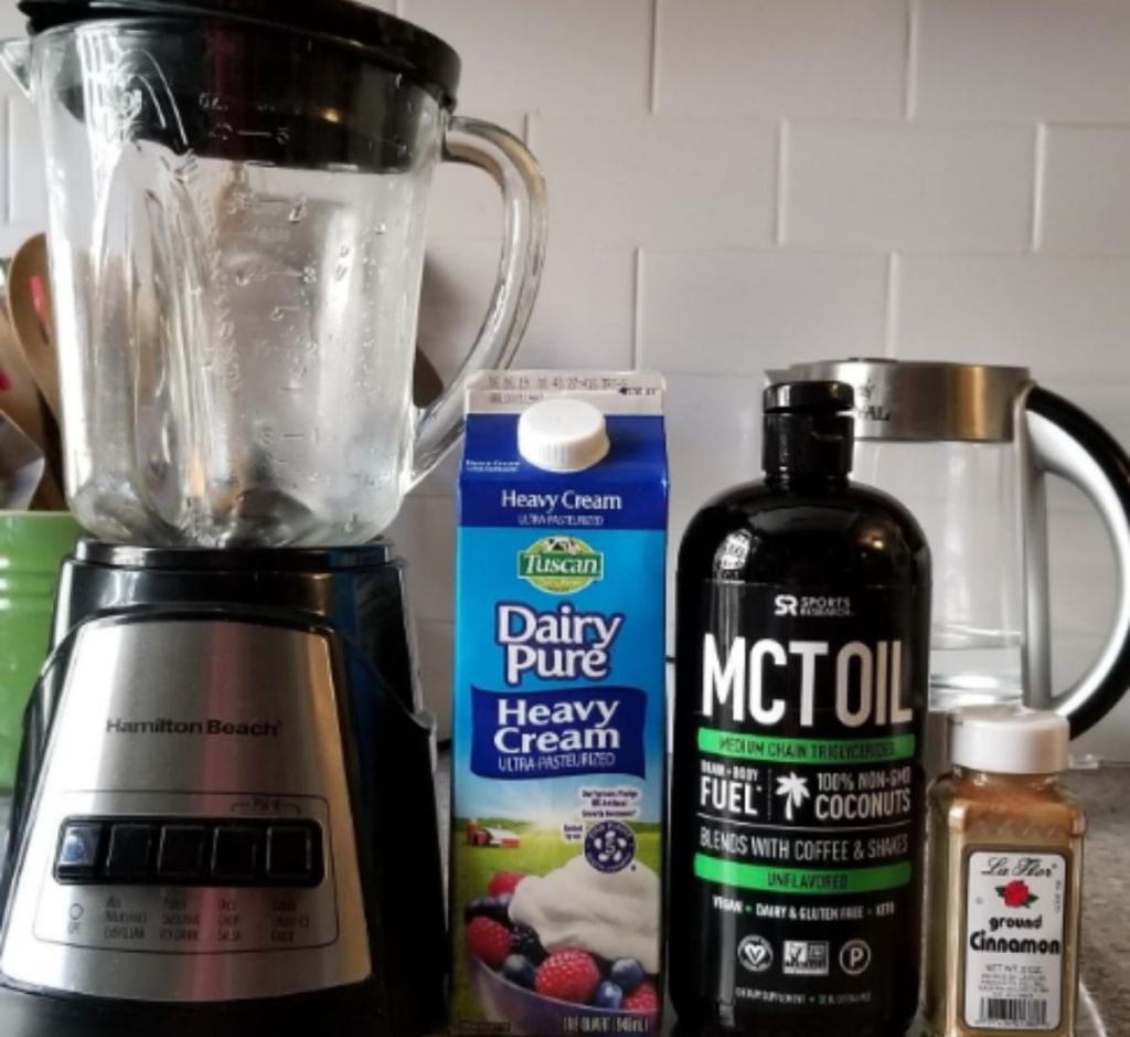 A blender on a counter next to MCT oil and heavy cream