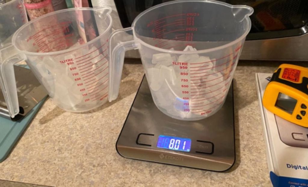 A digital food scale on a counter with a measuring cup full of ice on it