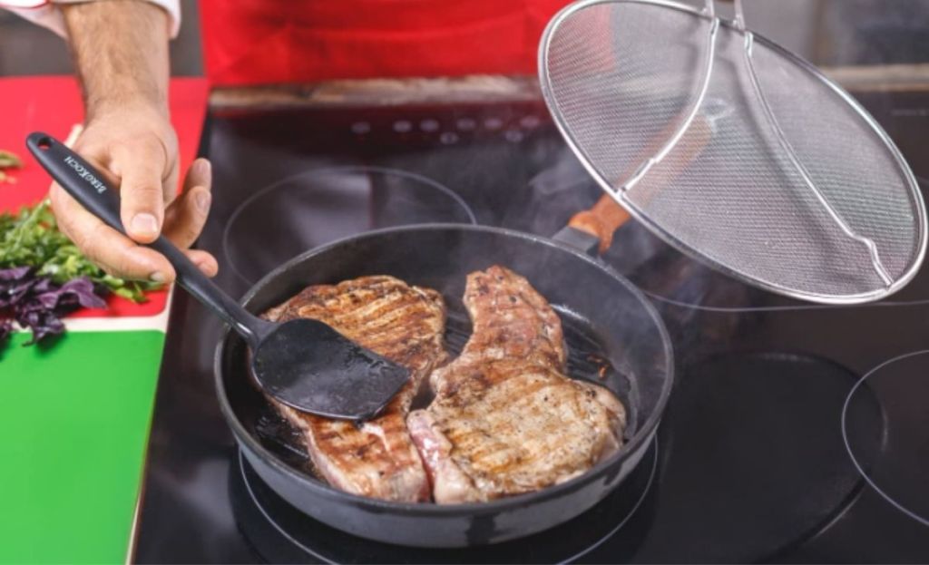 Someone cooking chicken in a pan and holding a grease splatter screen