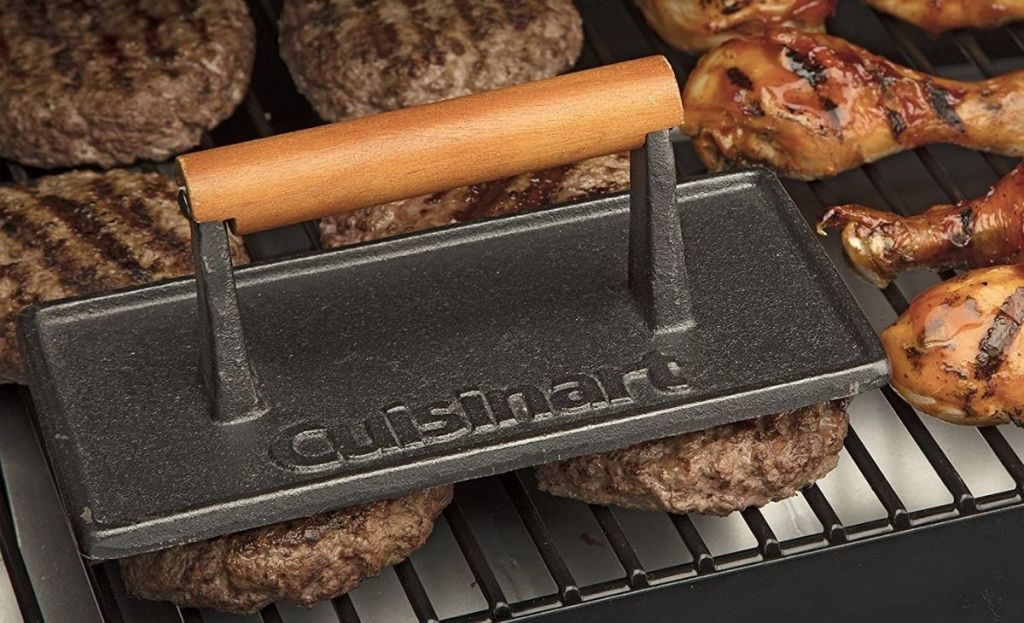 A grill press being used on patties on a grill