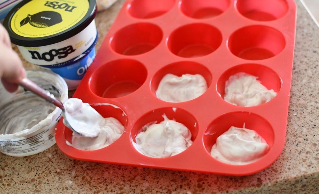 A hand placing scoops of yogurt in a silicone muffin tin