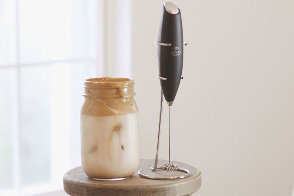 A milk frother next to a foamy coffee drink