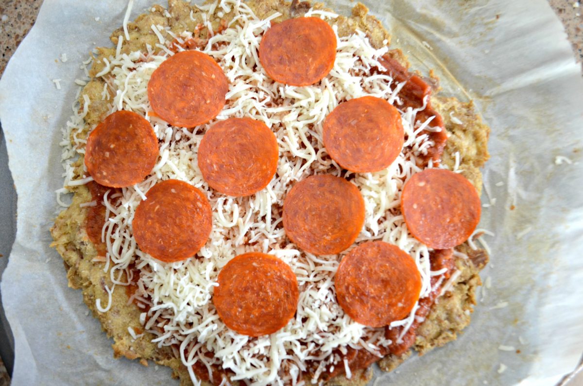 Keto chicken pizza crust topped with cheese and pepperoni.