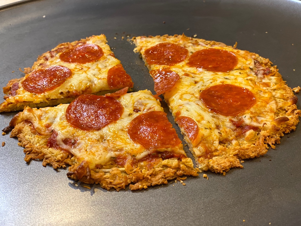 slicing a low carb pepperoni pizza made with keto chicken pizza crust