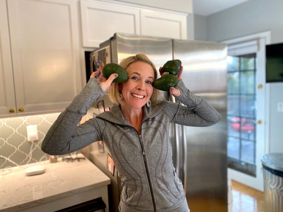 woman holding 3 avocados up to her face in the kitchen and smiling
