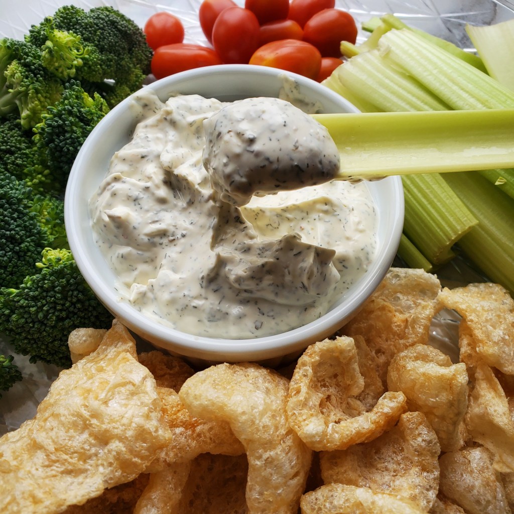 dipping a celery stick into homemade veggie dill dip 