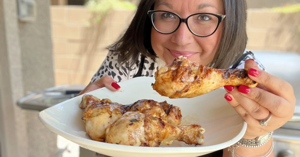 woman holding plate of grilled chicken drumsticks