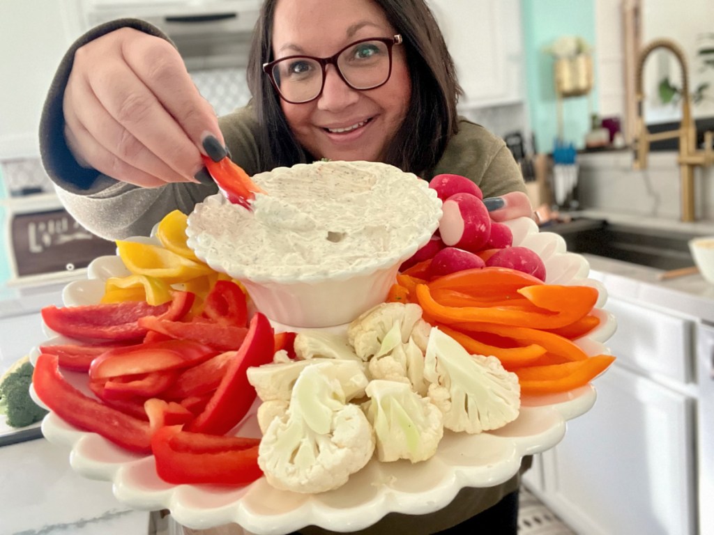 A woman holding up a platter with dill dip and veggies.