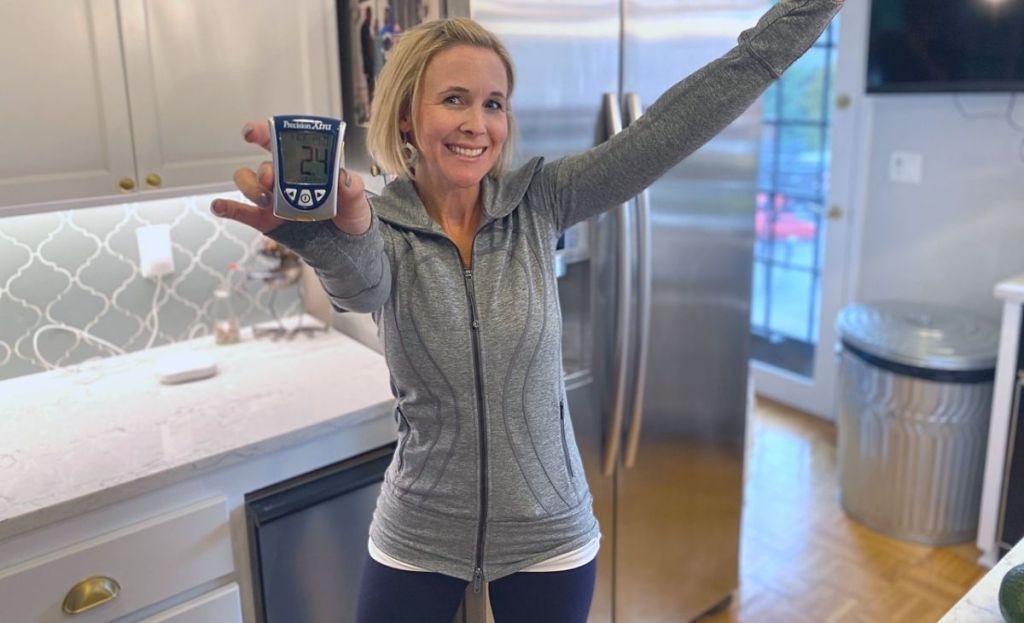 A woman holding a blood ketone meter in a kitchen