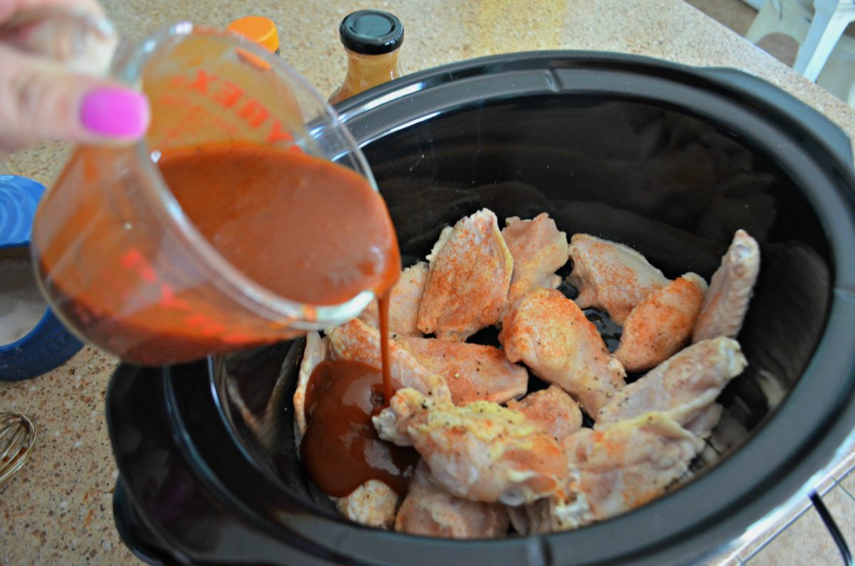 Slow Cooker Buffalo BBQ keto Wings - pouring the sauce over the wings