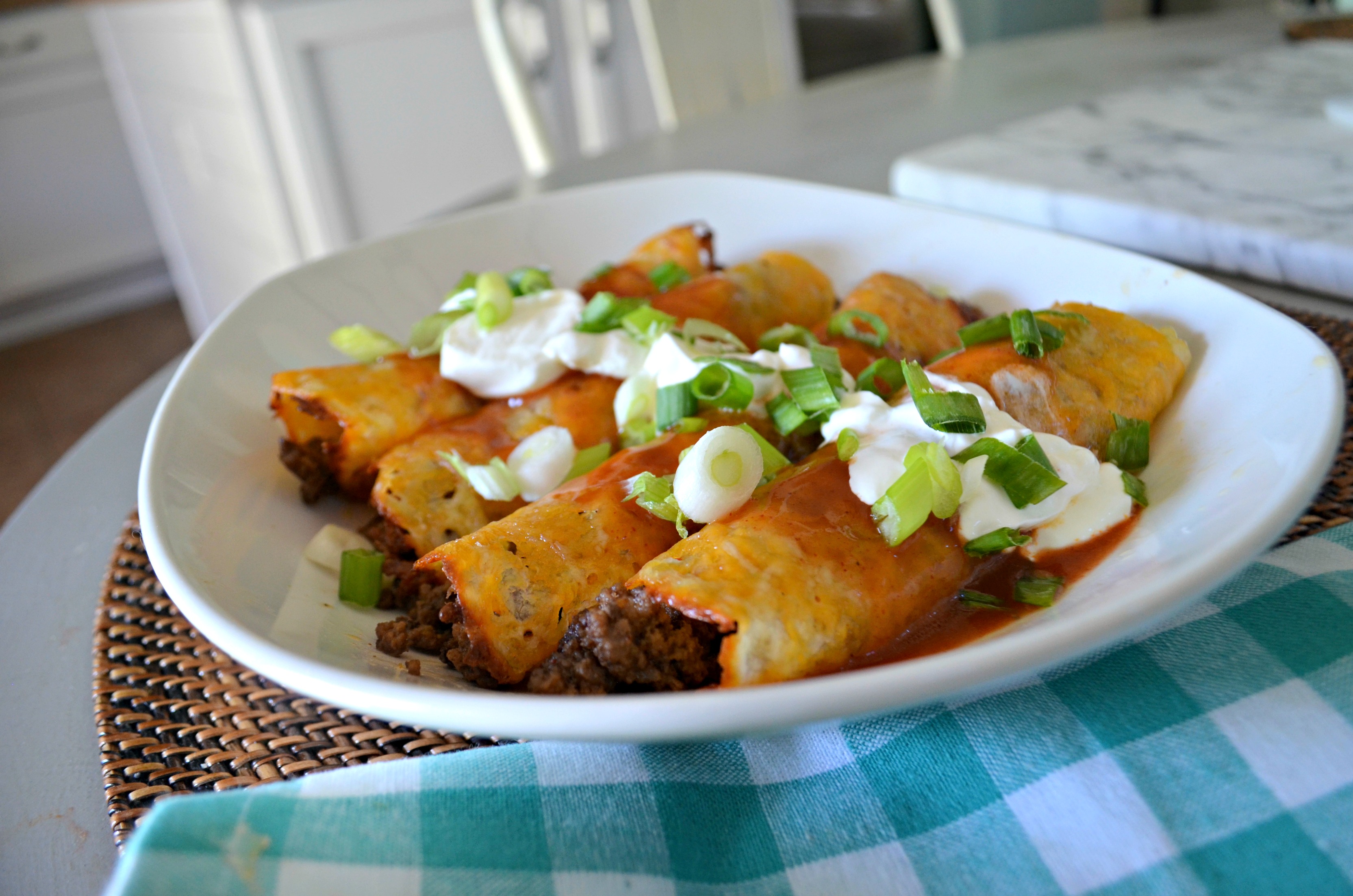 The ground beef keto enchiladas are arranged on a platter with sour cream and chopped green onion