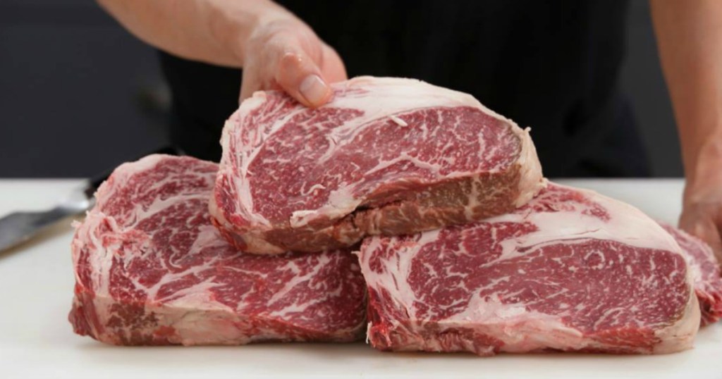 person holding uncooked steaks