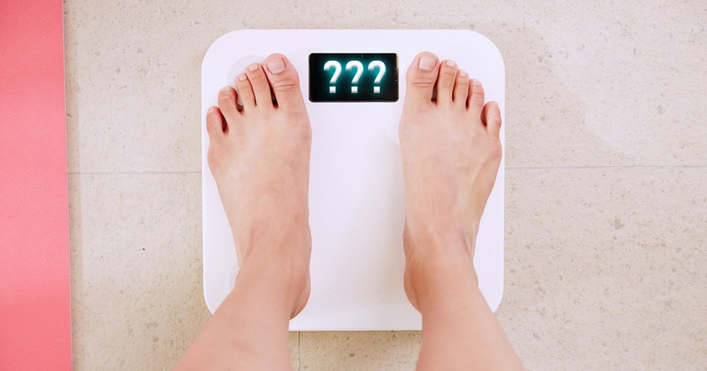 person on scale with question marks appearing for weight