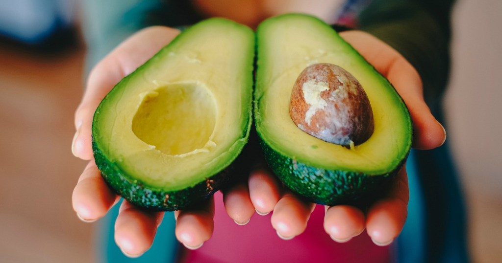 holding out avocado sliced in half with hands