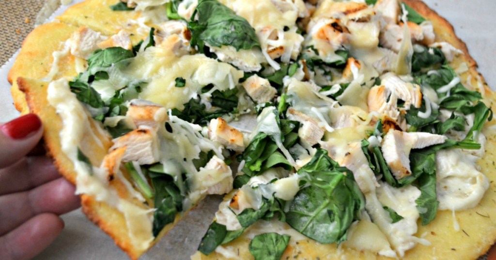 taking slice of keto spinach and chicken pizza 