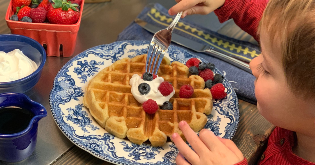 little boy eating keto waffle with whipped cream and berries 