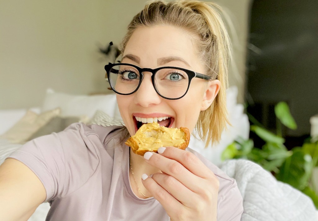 woman biting into bagel with miyokos creamery vegan cheese spread products on it