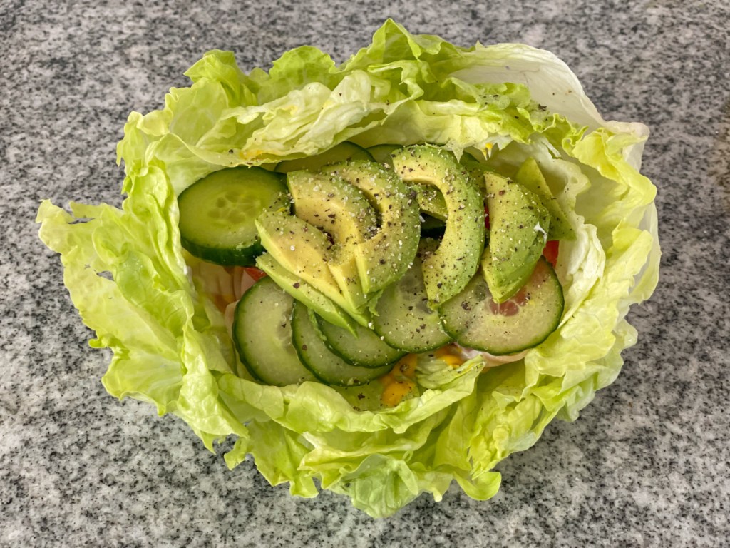 iceberg lettuce bowl with mayo, mustard, turkey lunch meat, tomato, cucumber, avocado, salt, and pepper