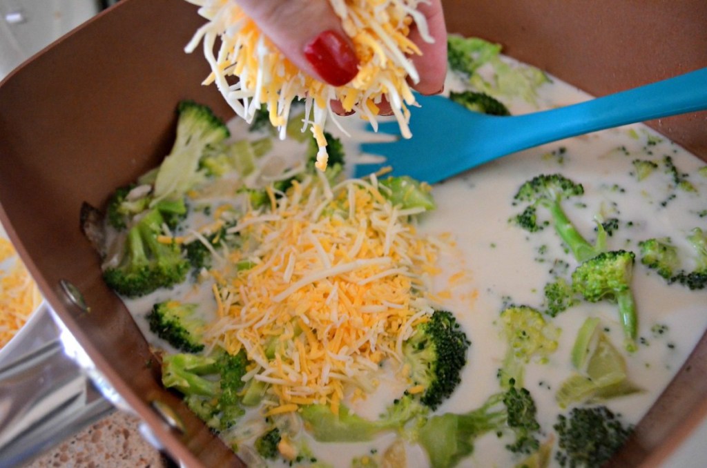 adding shredded cheese to broccoli soup in pan