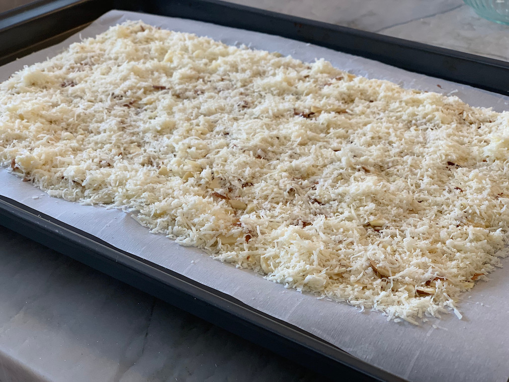 shredded parmesan cheese and almonds on sheet pan with parchment paper