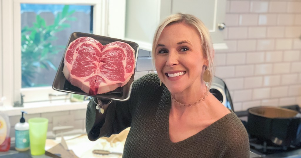 woman holding up ribeye steak shaped like a heart