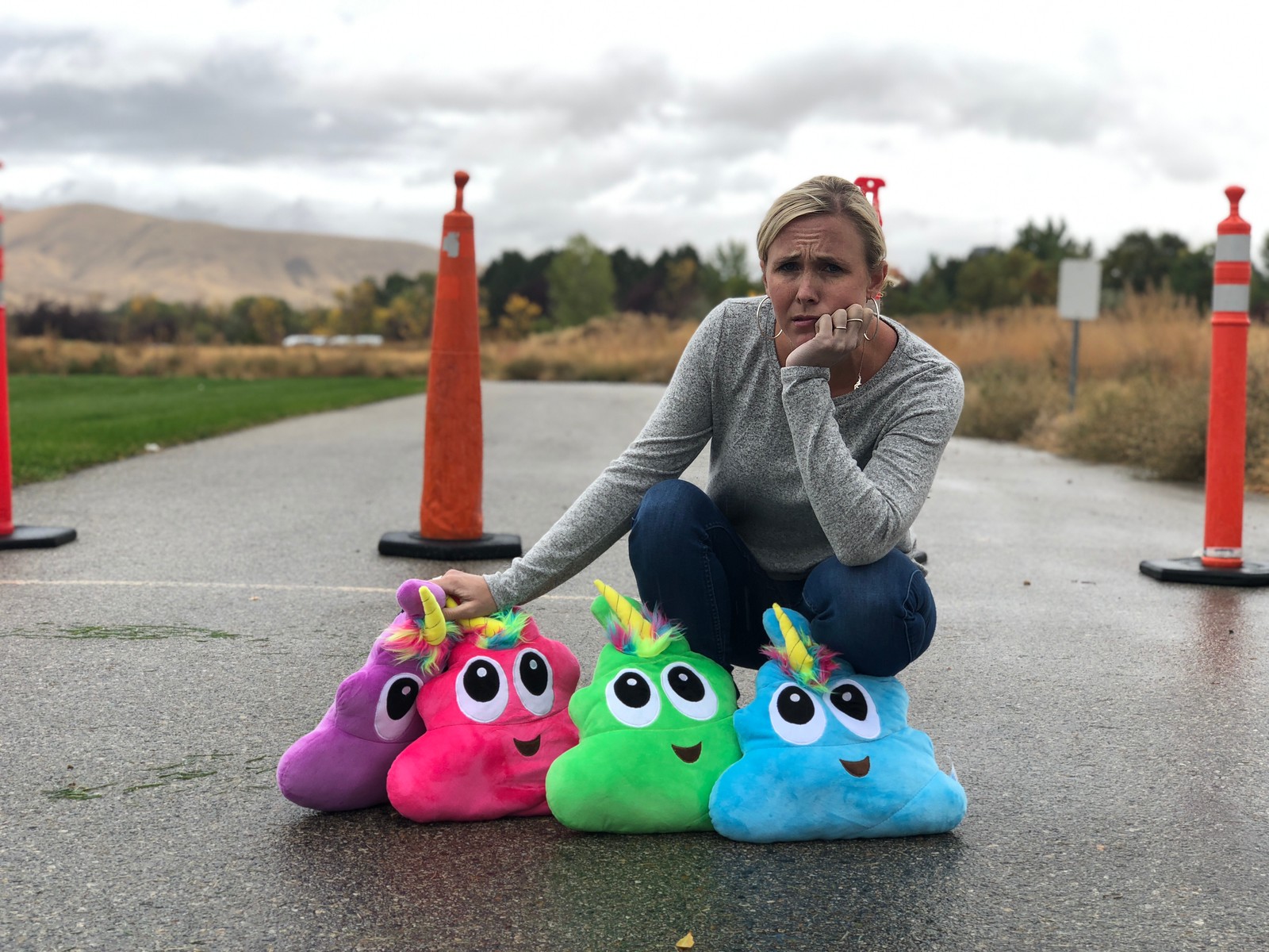 woman sitting in the road with construction cones around her and stuff poop emoji plushies