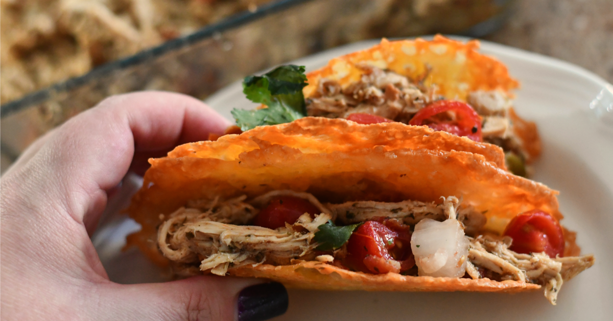 Keto Slow Cooker Shredded Chicken Tacos - a hand holding a delicious shredded chicken taco in a crispy cheese shell