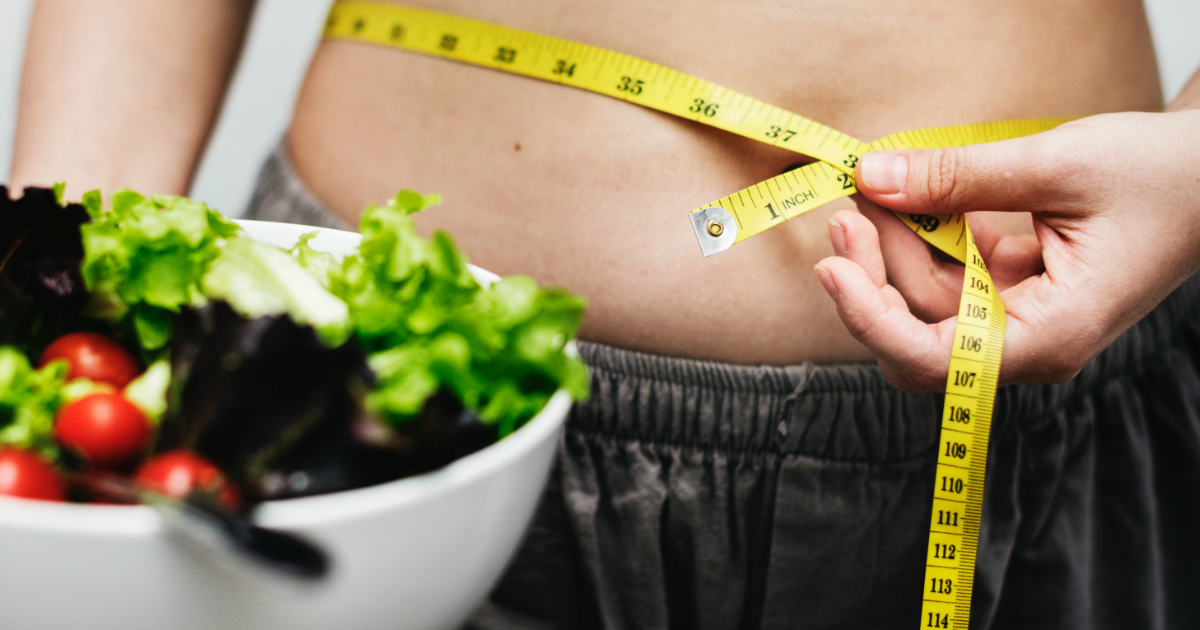 a woman holding a measuring tape around her waist near a salad