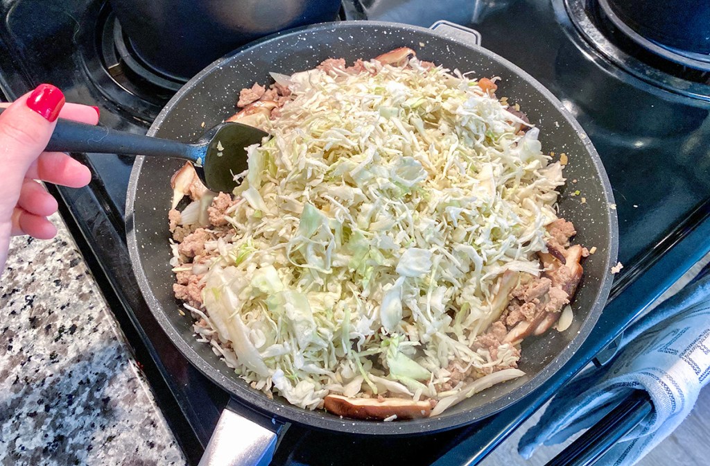 adding shredded cabbage to pan for keto egg roll in a bowl