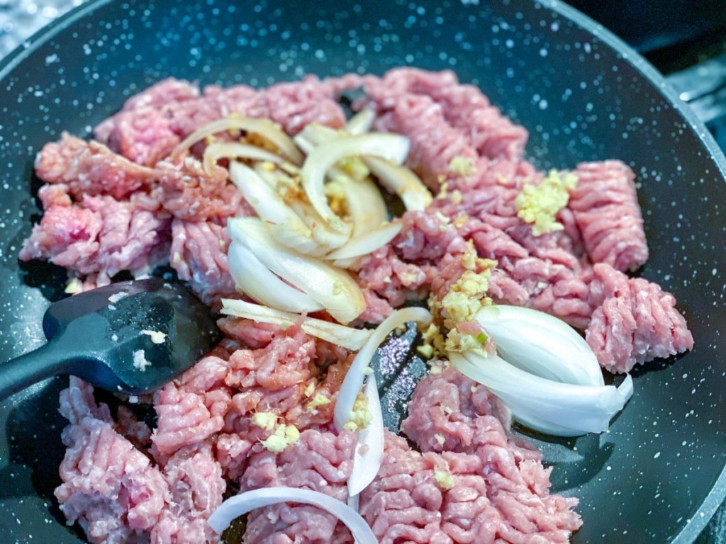 ground turkey cooking in a pan with onions, garlic, and ginger
