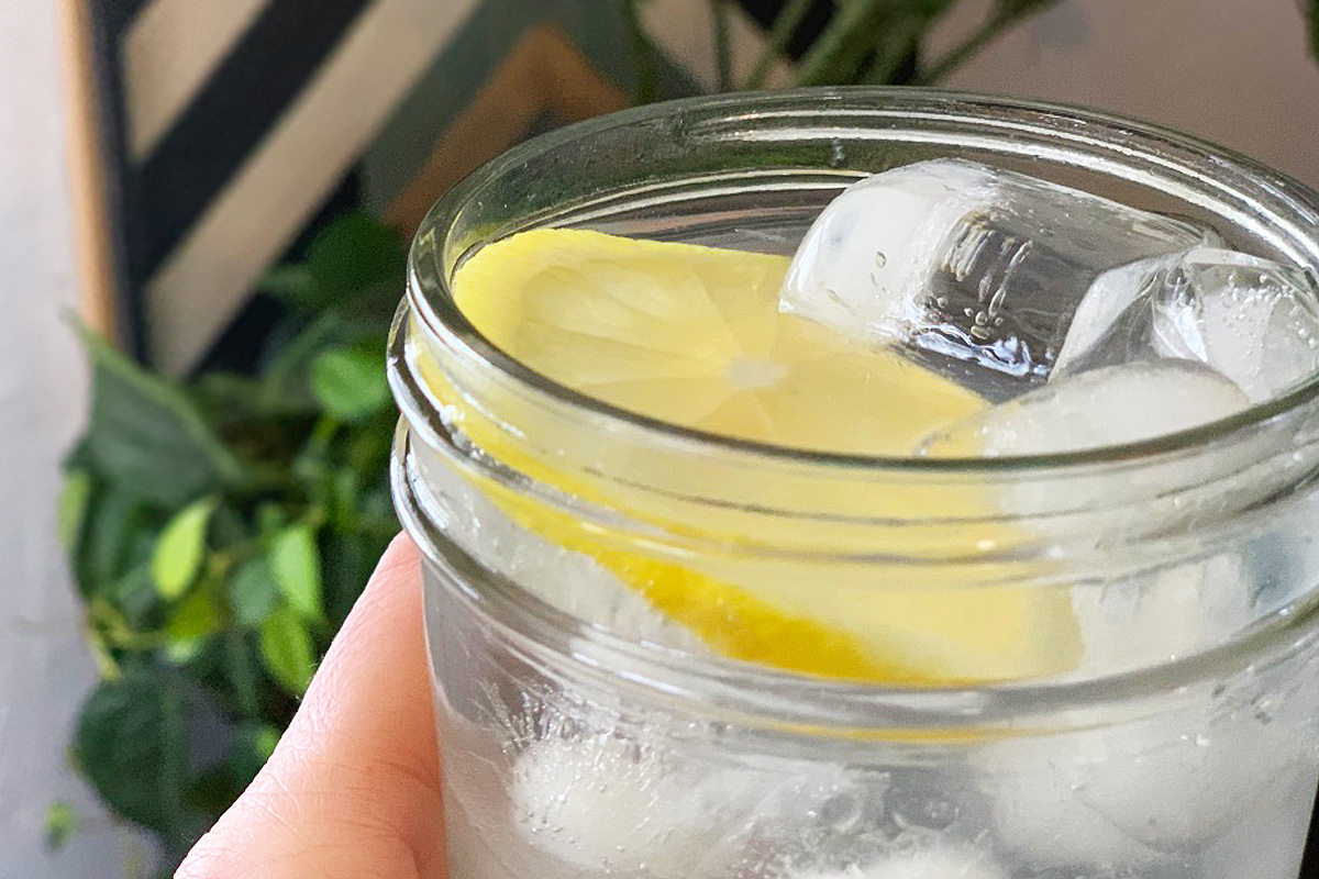 a mason jar glass filled with citrus water and garnished with a slice of lemon