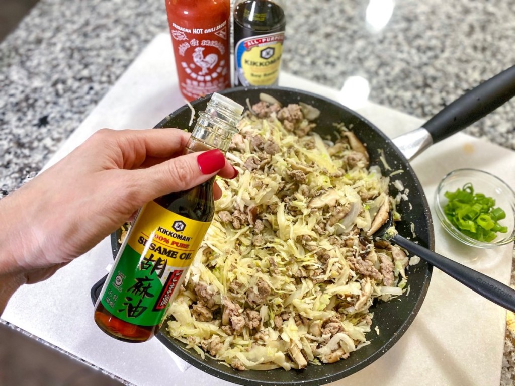 Sesame oil being poured into a pan of meat and cabbage