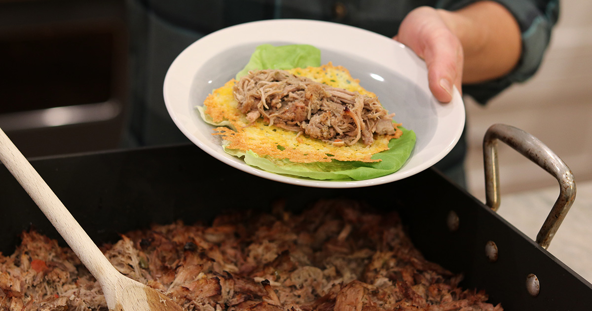 Pork carnitas being scooped onto a cheese shell