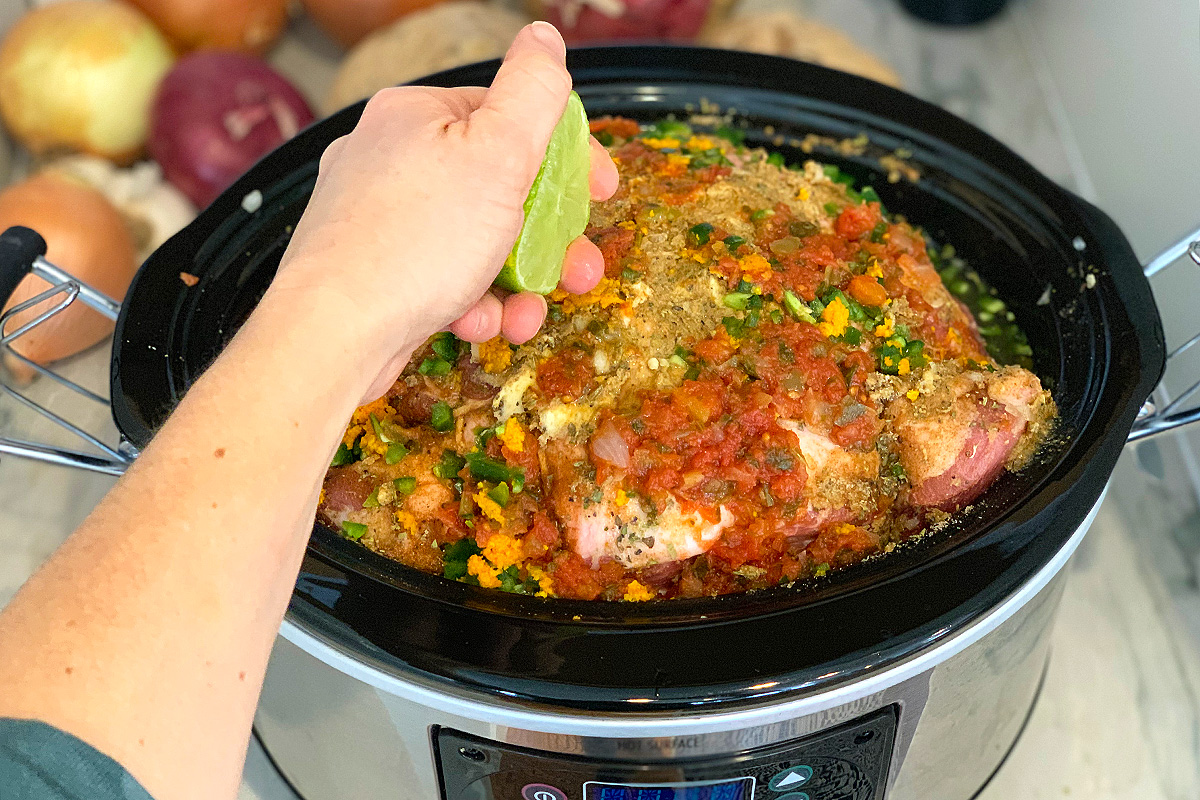 A slow cooker with pork roast topped with salsa and lime 
