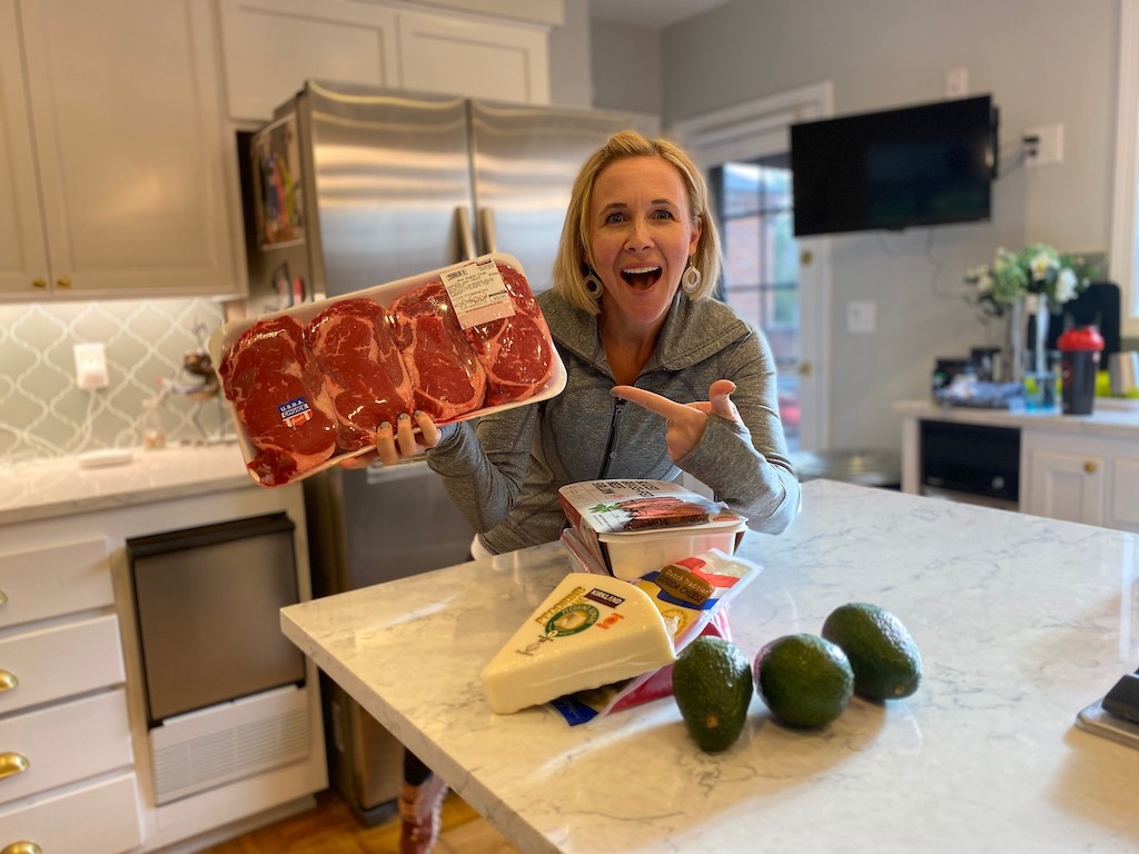 woman holding package of steaks with cheese and avocados on the counter