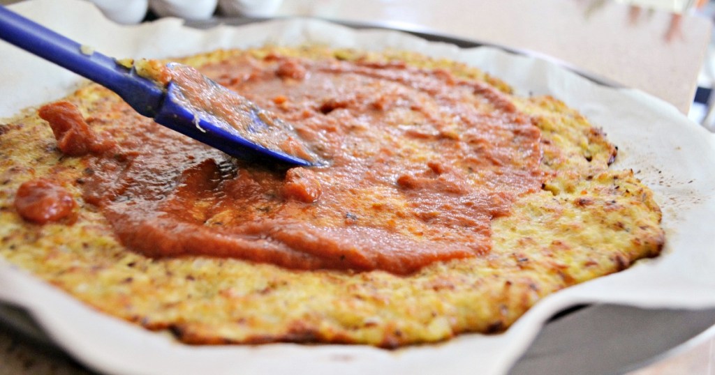 spreading sauce on cauliflower crust pizza