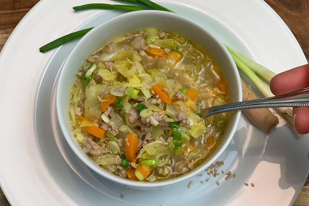 A hand holding a spoon ready to take a bite of egg roll soup