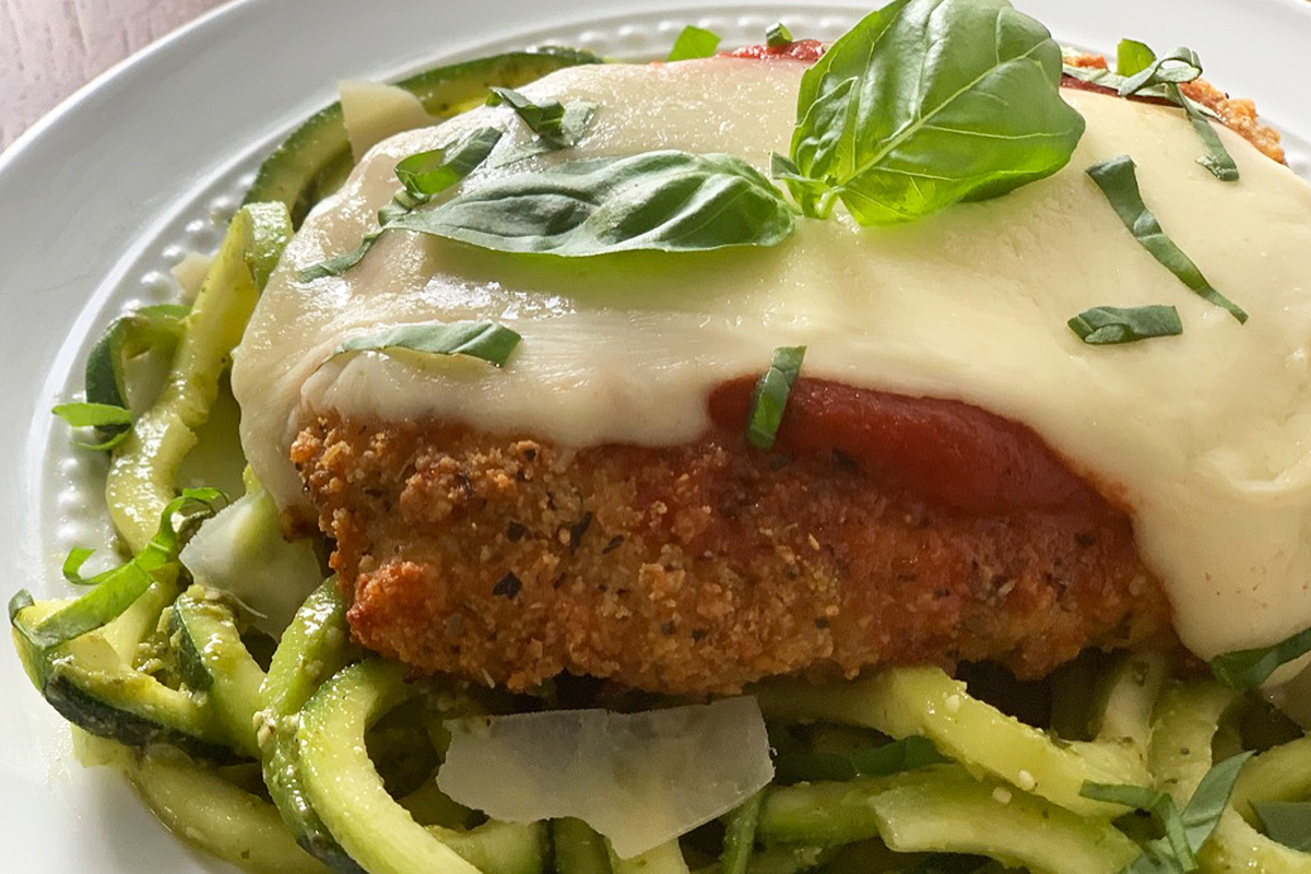 a close up of crispy chicken parmesan with melted cheese and fresh basil