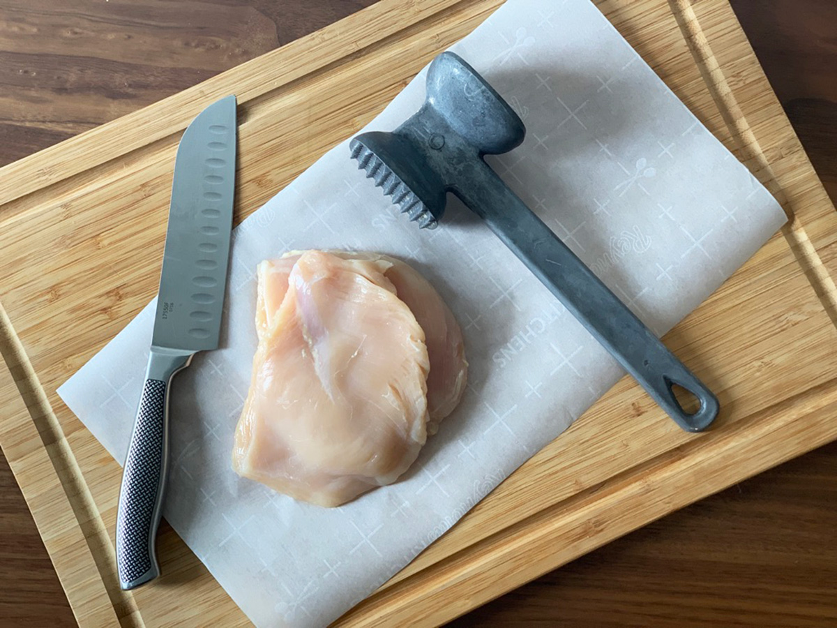 a cutting board with chicken breast ready to be pounded thin