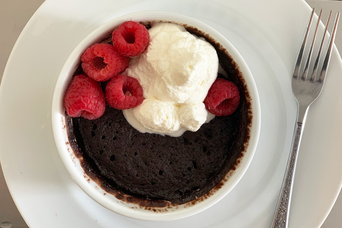 a fork beside a plate with chocolate cake, whipped cream, and berries 