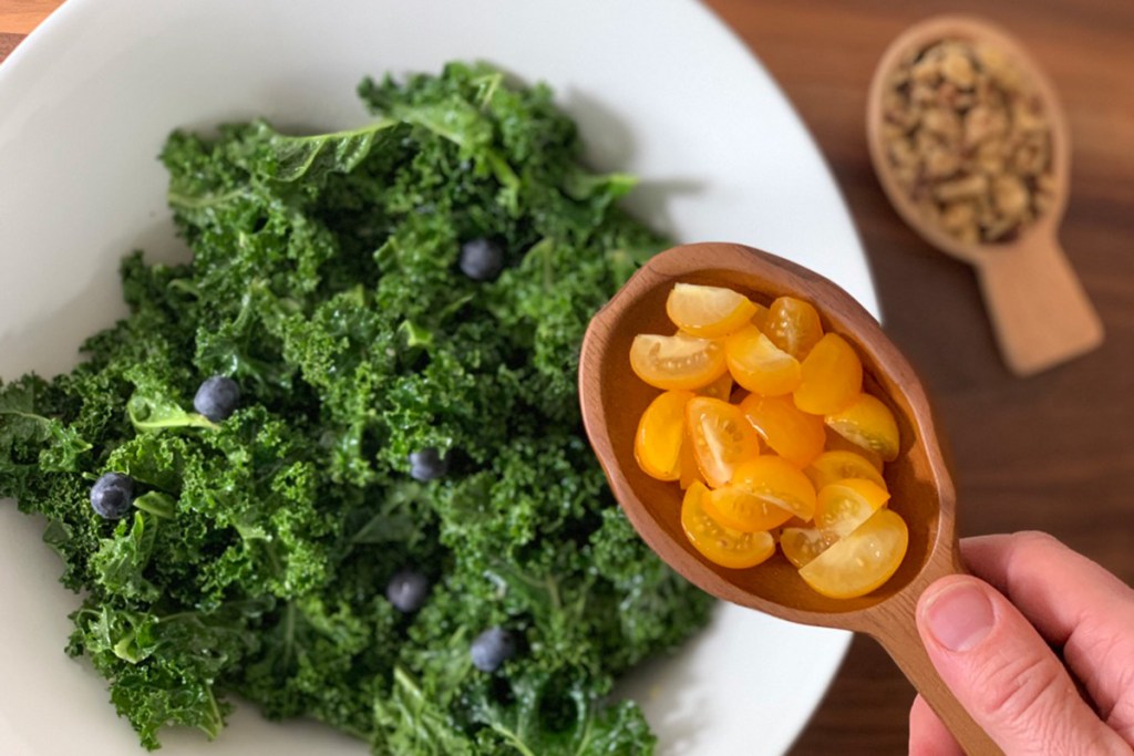 a wooden scoop with yellow tomatoes waiting to be added to kale salad