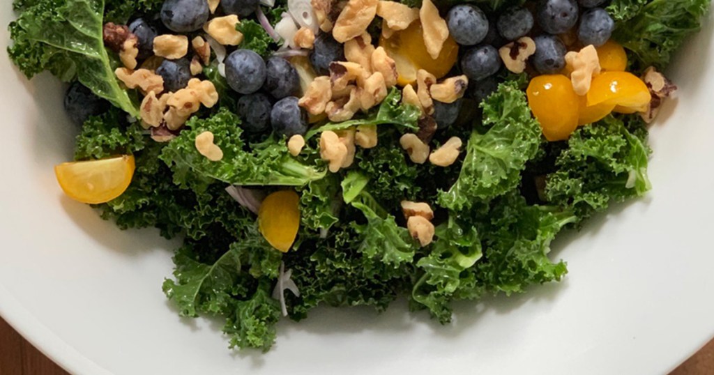 a large bowl of massaged kale salad with walnuts, blueberries and tomatoes on top