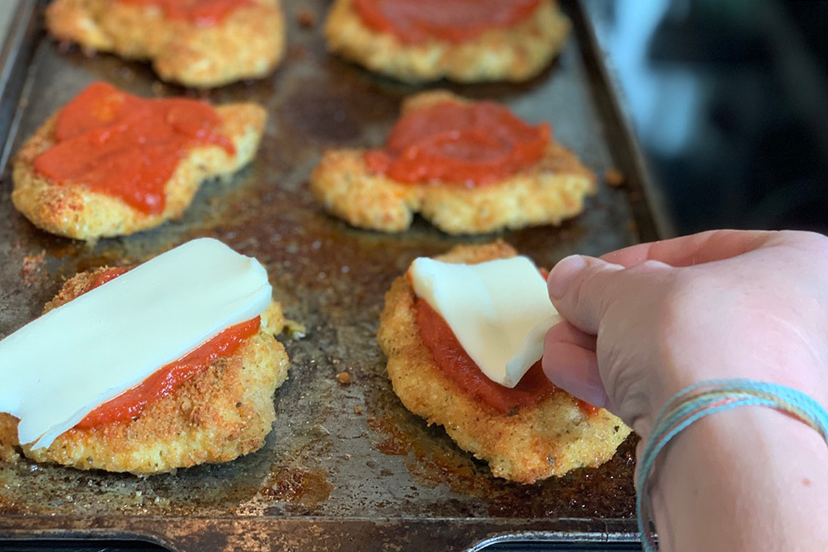 a pan of crispy keto breaded chicken breast brushed with sauce and topped with mozzarella cheese