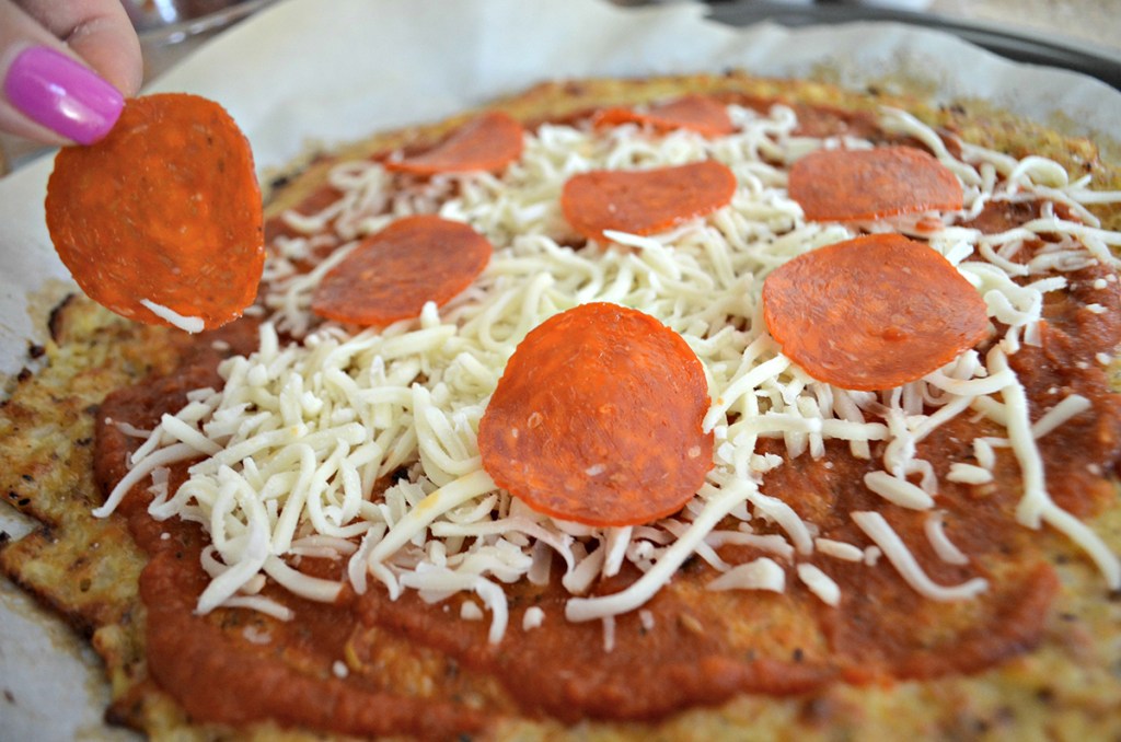 putting pepperonis on cauliflower crust pizza