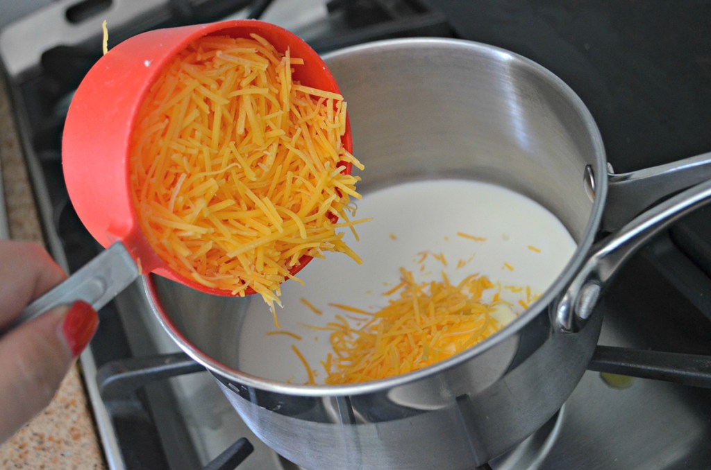 adding shredded cheese to cream in sauce pan