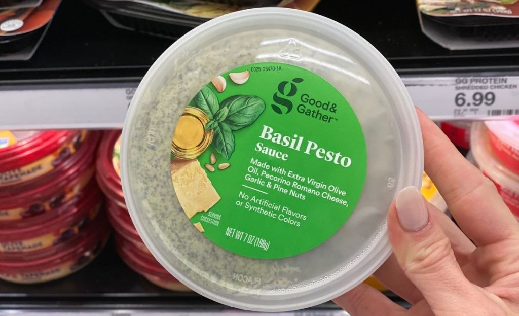 A hand holding a container of pesto sauce at a store