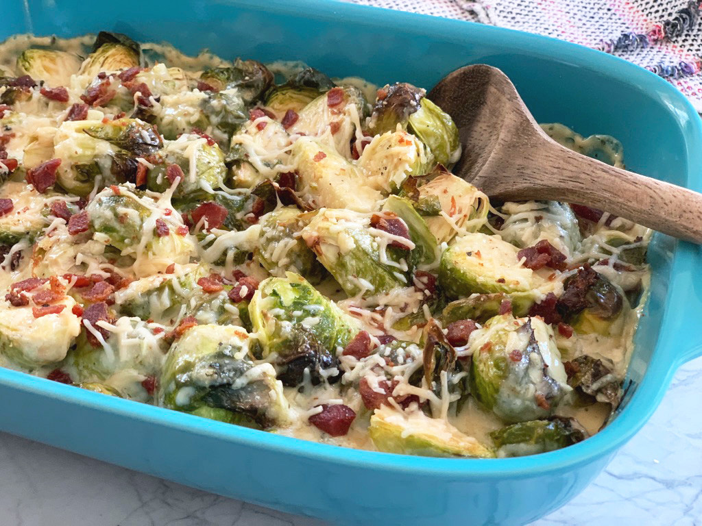 a serving spoon ready to scoop roasted Brussels sprouts in creamy Alfredo sauce