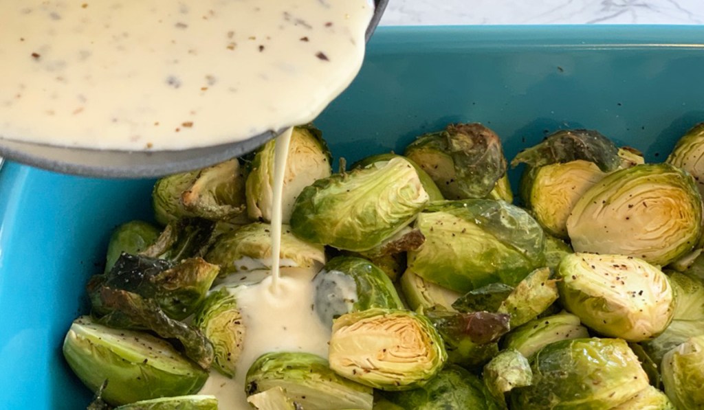 creamy Alfredo sauce being poured on a dish of roasted Brussels sprouts 