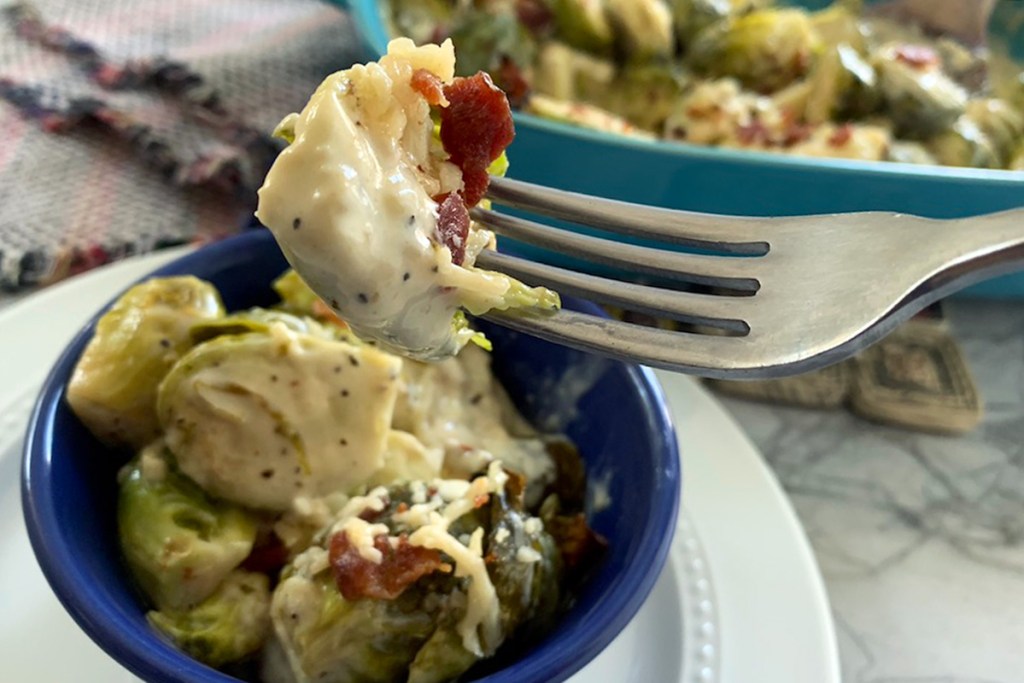 a fork with a roasted Brussels sprout, creamy Alfredo sauce, and bacon