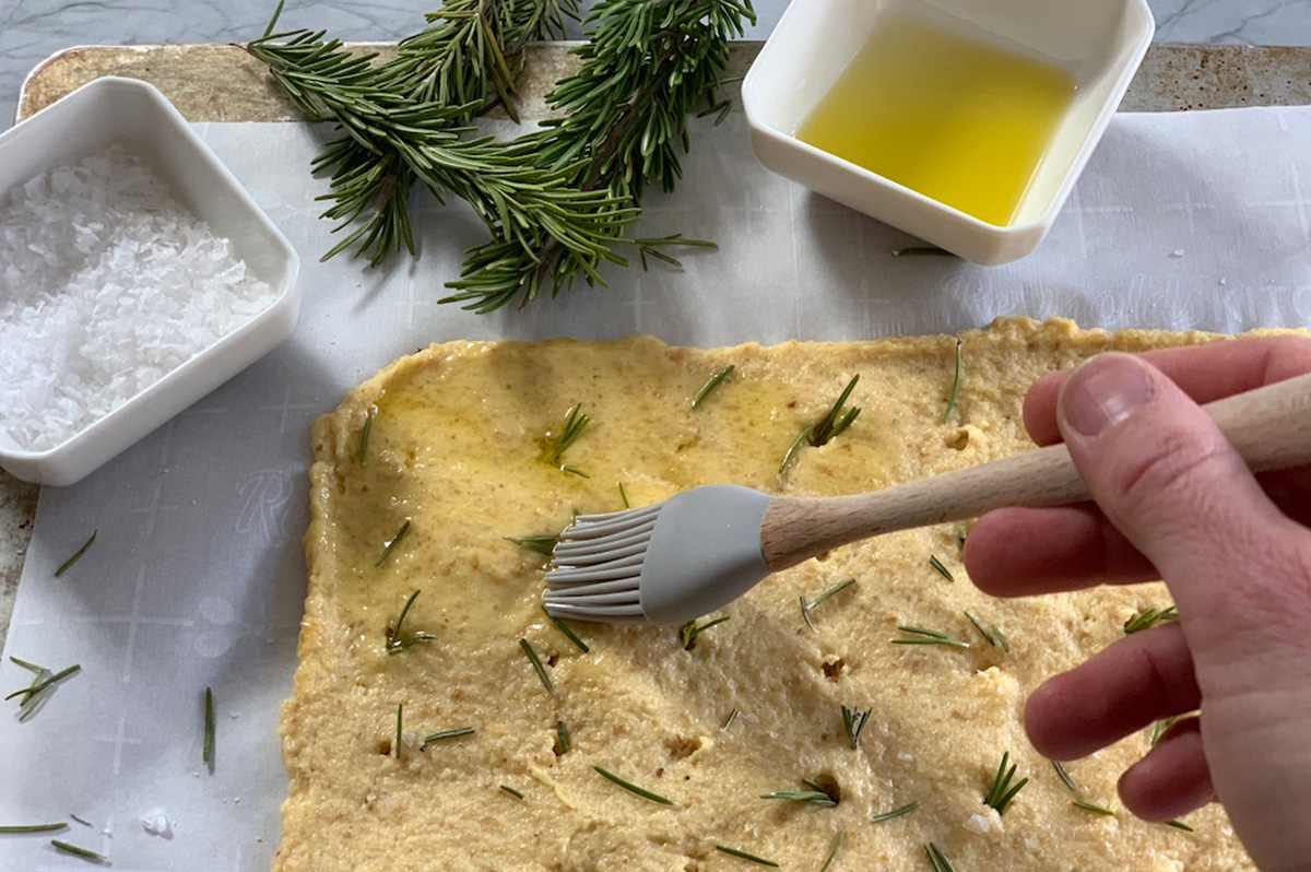 rosemary and sea salt focaccia bread dough being brushed with olive oil